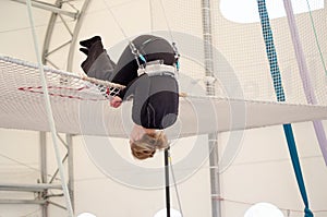 An adult female lands on a net, preparing to dismount at a on a flying trapeze school at an indoor gym. The woman is an amateur