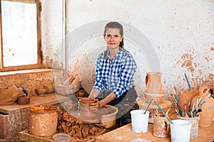 adult female potter working with clay on pottery wheel in atelier