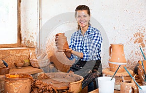 adult female potter working with clay on pottery wheel in atelier