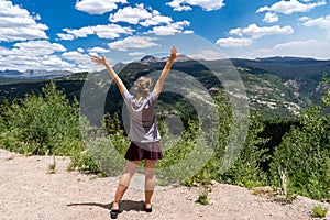 Adult female stands with arms raised, back facing viewer, along the Colorado Million Dollar Highway photo