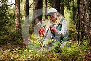 Adult female volunteer cleans garbage and plastic that pollutes environment in forest