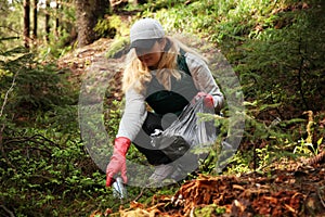 Adult female volunteer cleans garbage and plastic that pollutes environment in forest