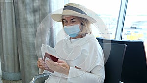 adult Female wearing a hat and a protective mask sits at the check-in counters in the airport terminal awaiting the