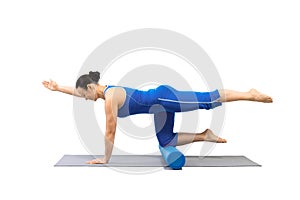 Adult fit woman does bird dog drill with one leg and arm up and foam roller under her knees. Classic pilates exercise