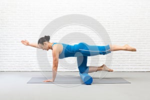 Adult fit woman practice pilates with props in fitness studio indoor, bird dog drill with one leg up and foam roller