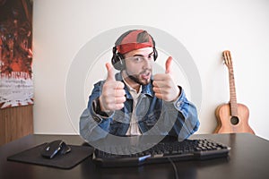 Adult gamer sits at home with a computer, shows a thumbs up and looks into the camera photo