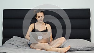 Adult girl chatting online on networks on notebook. Young woman sitting on bed, using laptop notebook, looking at screen and typin