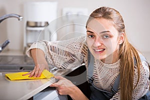 Adult girl dusting surfaces in residential kitchen