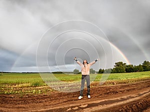 An adult girl in a field with a stormy sky with clouds and grey rainbow. A woman having fun outdoors on rural and rustic