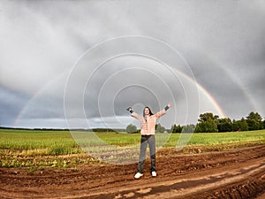 An adult girl in a field with a stormy sky with clouds and grey rainbow. A woman having fun outdoors on rural and rustic