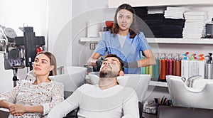 Adult girl hairdresser washing hair of positive man in salon