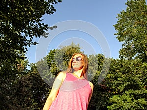 Adult girl with long blond hair in sunglasses looks into the distance, smiling. Portrait of a young woman against the blue sky and