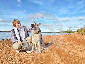 Adult girl with shepherd dog taking selfie near water of lake or river. Middle aged woman and big pet on nature