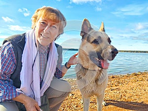 Adult girl with shepherd dog taking selfie near water of lake or river. Middle aged woman and big pet on nature