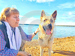 Adult girl with shepherd dog taking selfie near water of lake or river. Middle aged woman and big pet on nature