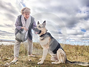 Adult girl with shepherd dog taking selfies in a field. Middle aged woman and big shepherd dog on nature. Friendship