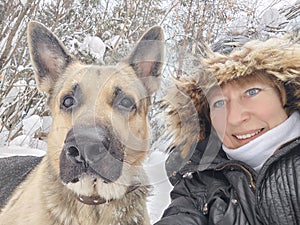 Adult girl with shepherd dog taking selfies in a winter forest. Middle aged woman and big shepherd dog on nature in cold