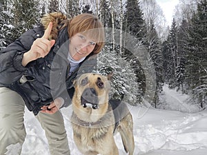 Adult girl with shepherd dog taking selfies in a winter forest. Middle aged woman and big shepherd dog on nature in cold