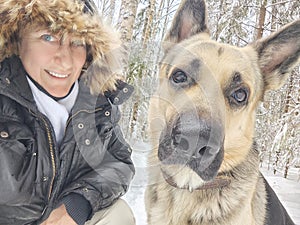 Adult girl with shepherd dog taking selfies in a winter forest. Middle aged woman and big shepherd dog on nature in cold