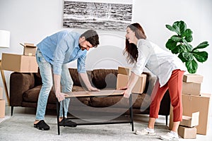 Adult girlfriend and boyfriend move in appartment, carrying table