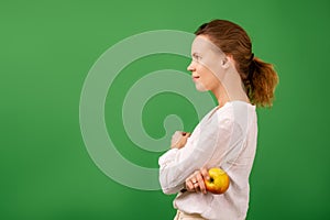 Adult good looking woman in white shirt holds fresh apple on green background. Healthy eating, vegetarianism, healthy appearance