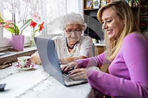 Adult granddaughter teaching her elderly grandmother to use laptop