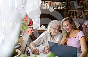 Adult granddaughter teaching her elderly grandmother to use laptop