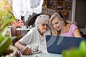 Adult granddaughter teaching her elderly grandmother to use laptop