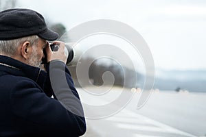 An adult gray-haired man with a camera on a mountain road in foggy inclement weather. Copy space. Selective focus