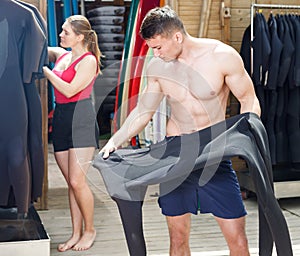 Adult guy surfer choosing surfing suit for rent