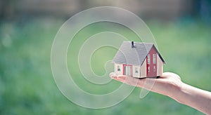 Adult hand is holding red house model, outdoors. Concept for new home, property and estate. Text space