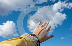 Adult hand reaching out towards the sky. Hand touch the blue sky with clouds