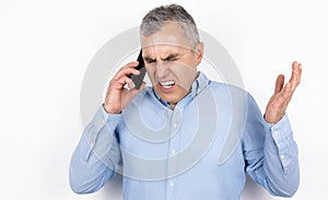 Adult handsome man with grey hair wearing blue shirt having phone conversation looks angry standing on  white background,