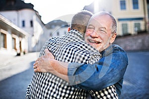 An adult hipster son and his senior father in town, hugging.