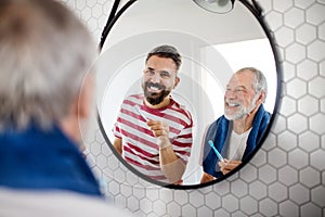 An adult hipster son and senior father in bathroom indoors at home, brushing teeth.