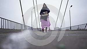 Adult homeless woman stay on the bridge near the river port in cold windy grey weather asking for help and begging money