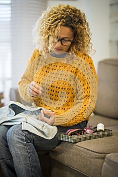 Adult housewife at home repairing clothes with cord - sailor and sew jeans jacket -beauiful young woman in activiy at home sitting