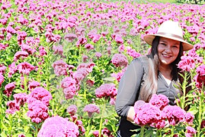 Adult latin woman with hat walks in field of red flowers, flower for day of the dead in Mexico