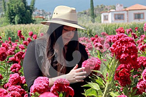 Adult latin woman with hat walks in field of red flowers, flower for day of the dead in Mexico