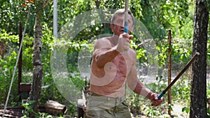 Adult male athlete showing fighting techniques with wooden sticks outdoor. Older sportsman demonstrating wing chun kung