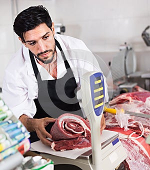 Adult male butcher in uniform is weighing meat