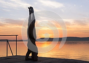 Adult male doing yoga exercises at sunset, head stand