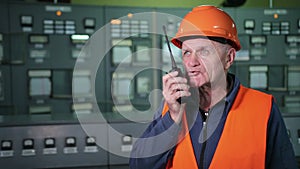 Adult male engineer in protective helmet, workwear using walkie talkie