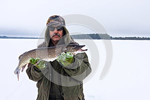 Adult male fisherman holds a large pike fish. winter fishing