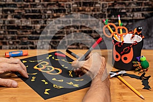 Adult male hands drawing on a sign covered in Yellow Bloodshot eyes for Halloween.  Other crafts and supplies scattered on the