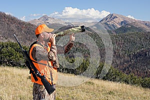 Adult elk hunter blowing bugle in mountains photo