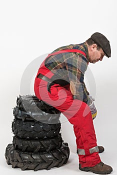 adult male mechanic sitting tiredly on a stack of wheels