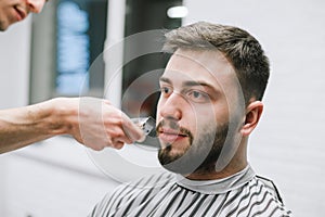 Adult male model with beard trimming at barber shop. Close up portrait of a client doing hairstyle in light barbershop. Male