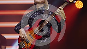 Adult male musician plays electric guitar at concert in light of red spotlights. Close-up