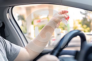 Adult male person throwing out paper fast food snack wrap garbage in window driving car on sunny day. Man hand tossing waste